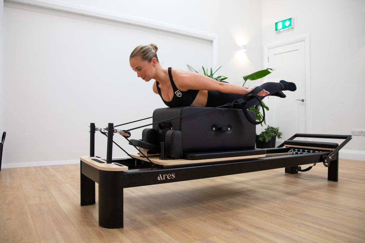 Woman using a Pilates reformer machine in a studio setting