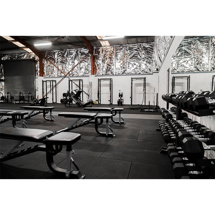 Gym interior with weight benches and dumbbells on a dark floor.