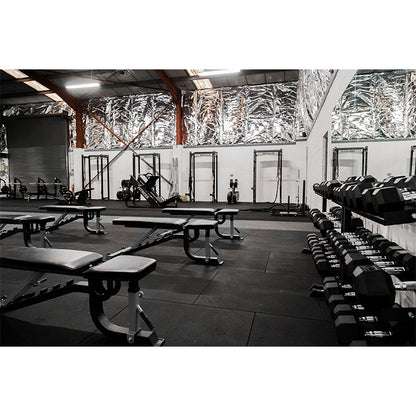 Gym interior with weight benches and dumbbells on a dark floor.