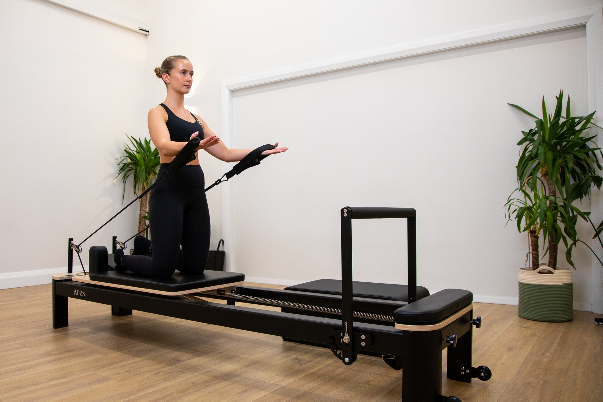 Woman exercising on a Pilates reformer machine in a studio setting.