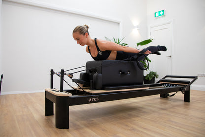 Woman using a Pilates reformer machine in a studio setting